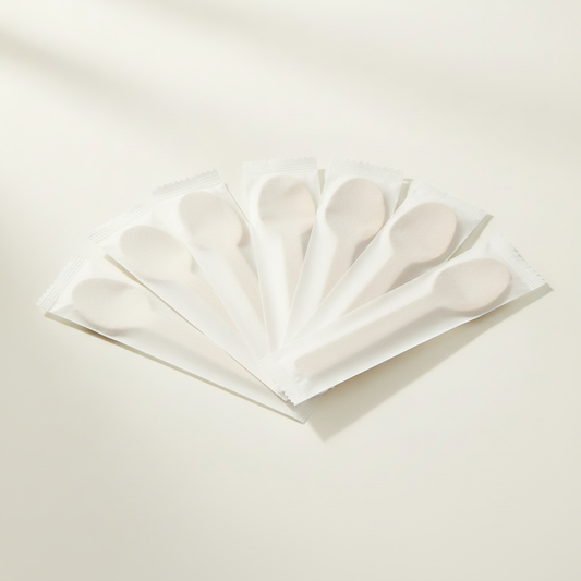 Individually wrapped wooden spoons in opaque white paper sleeves on a clean white background